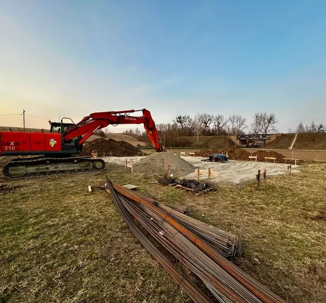 Wytyczone ławy fundamentowe i dostarczone pręty zbrojeniowe na placu budowy o zachodzie słońca