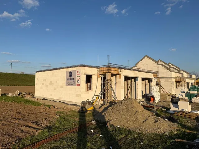 Zbrojenie wieńca żelbetowego przygotowane do betonowania, obok szalunek słupa podcienia, w tle kolejny budynek ze ścianami szczytowymi