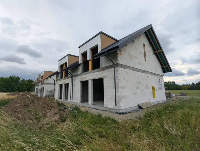 Narożnik budynku dwulokalowego z ukończonym dachem, w tle kolejne budynki osiedla