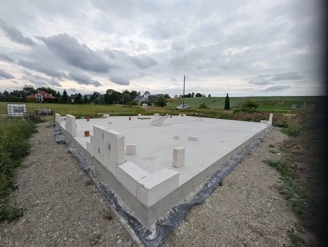 Zabetonowana płyta fundamentowa kolejnego budynku z pierwszymi bloczkami ścian i wyprowadzonymi przejściami instalacyjnymi