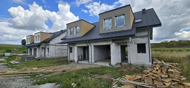 Budynek dwulokalowy z lukarnami od strony podjazdu, za nim kolejny budynek z rusztowaniem przy ścianie