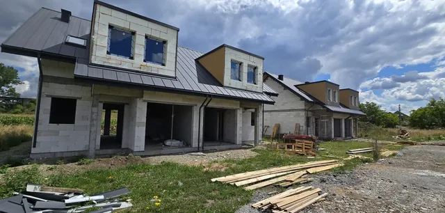 Lukarny w trakcie ocieplania płytami styropianu, z zamontowanymi oknami; w głębi kolejne budynki z rusztowaniami